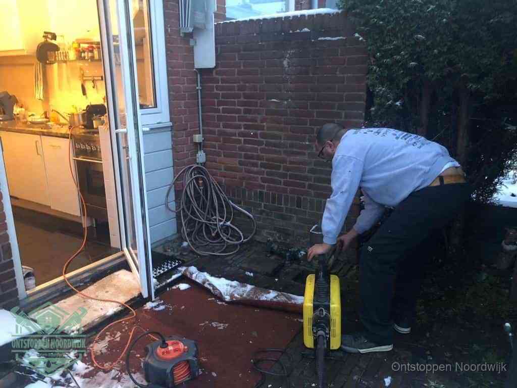 Een monteur werkt buiten bij een open riool-/grondput met een elektrische ontstoppingsmachine om een verborgen afvoerprobleem op te sporen in Noordwijk
