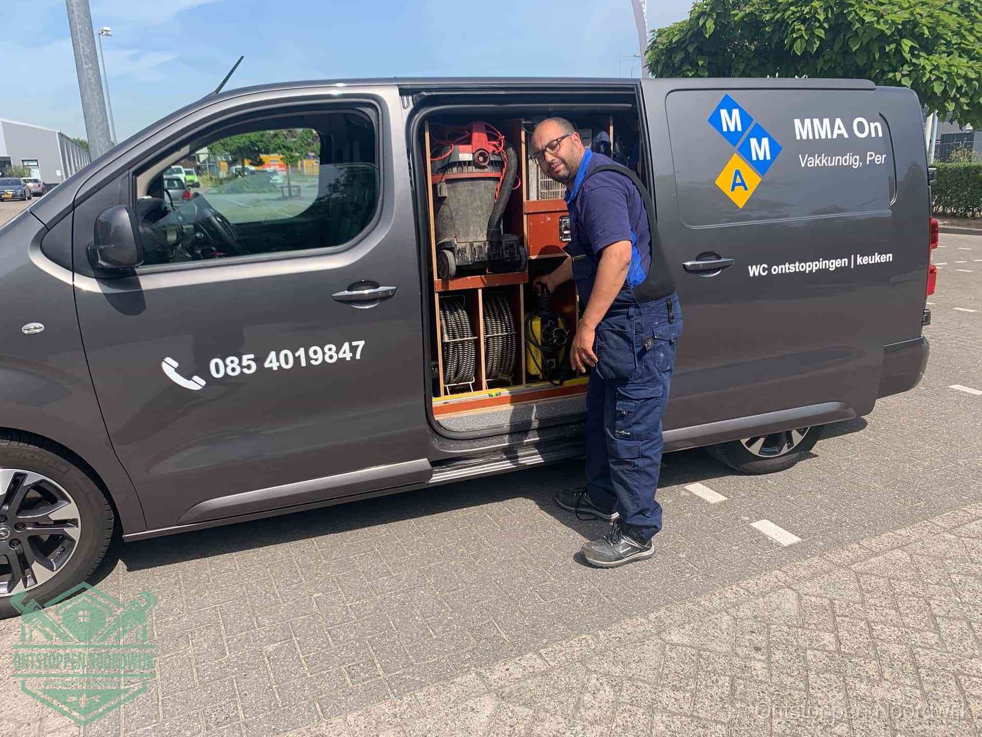 Een monteur bij de open schuifdeur van zijn bedrijfsbus op een parkeerplaats, klaar om de oorzaak van terugkerende afvoerverstoppingen aan te pakken in Noordwijk