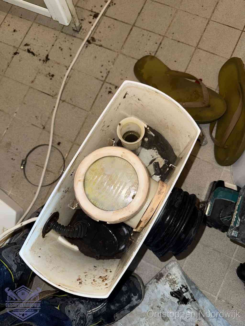 Een gedemonteerde toiletpot op de vloer met ontstoppingsveer en gereedschap ernaast, het verwijderen van een vastzittend voorwerp uit de wc in Noordwijk
