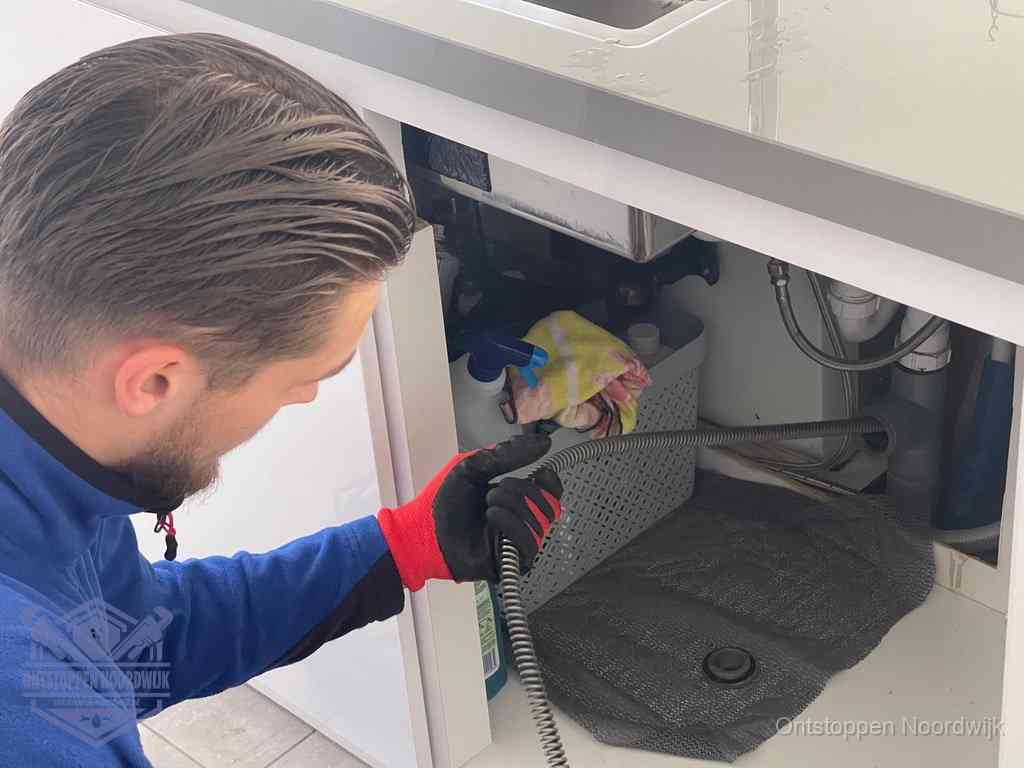 Een monteur voert een flexibele ontstoppingsveer in de afvoer om een verstopping voorbij de bocht van het toilet te bereiken in Noordwijk
