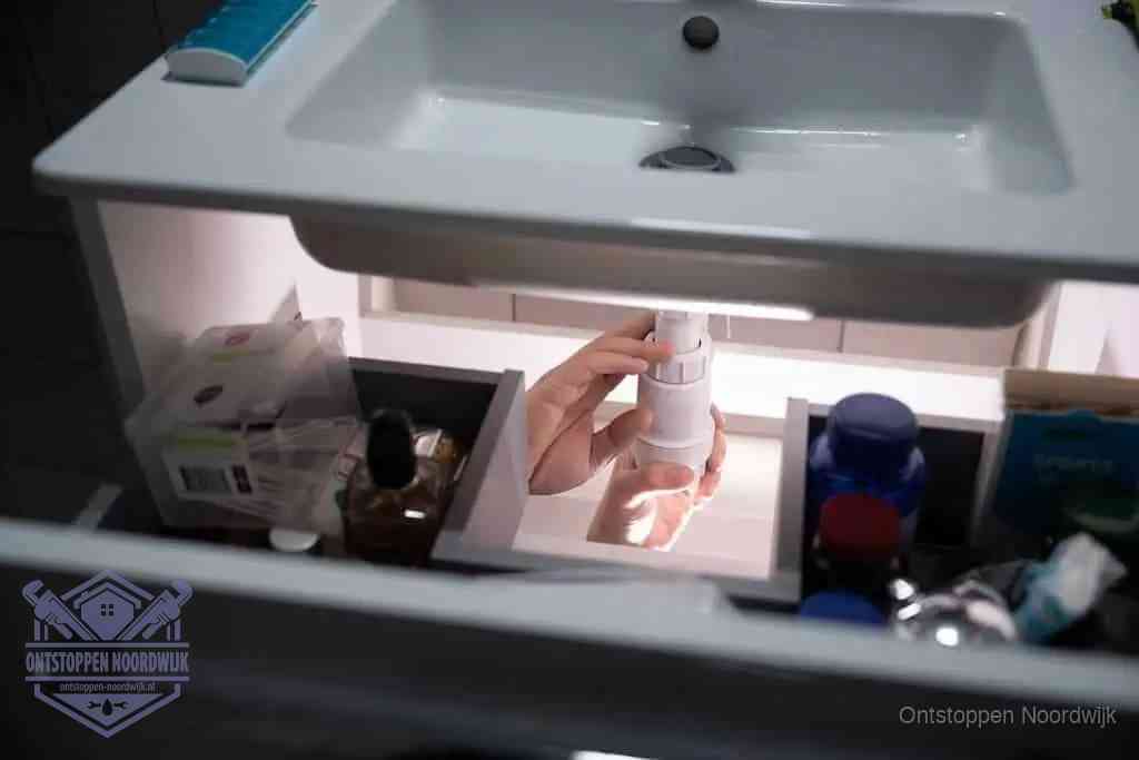 Een pompfles met zeep boven een wastafel in de toiletruimte, de warm water en afwasmiddel-methode om de wc te ontstoppen in Noordwijk