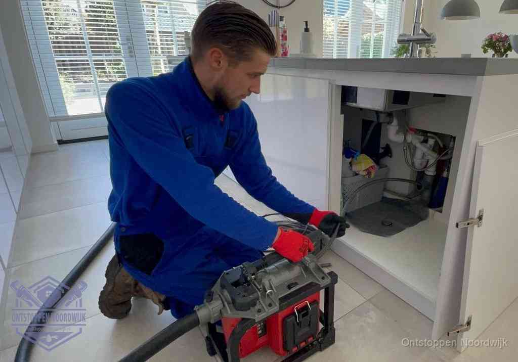 Een monteur voert een professionele elektrische ontstoppingsmachine in de afvoer onder de spoelbak tijdens het gootsteen ontstoppen in Noordwijk