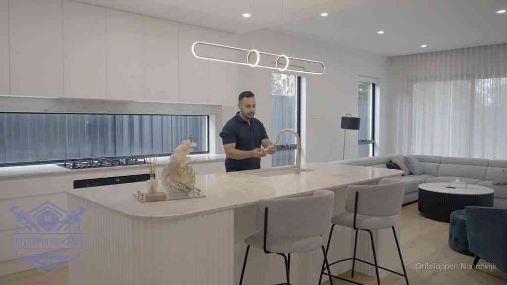 Een bewoner bij de keukenspoelbak die zelf aan de slag gaat met een verstopte gootsteen in Noordwijk